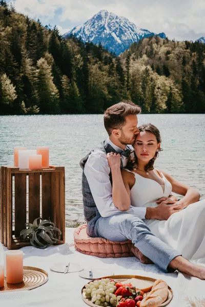 Das Brautpaar beim Hochzeits-Picknick am Bergsee vor Alpenpanorama mit Kerzen